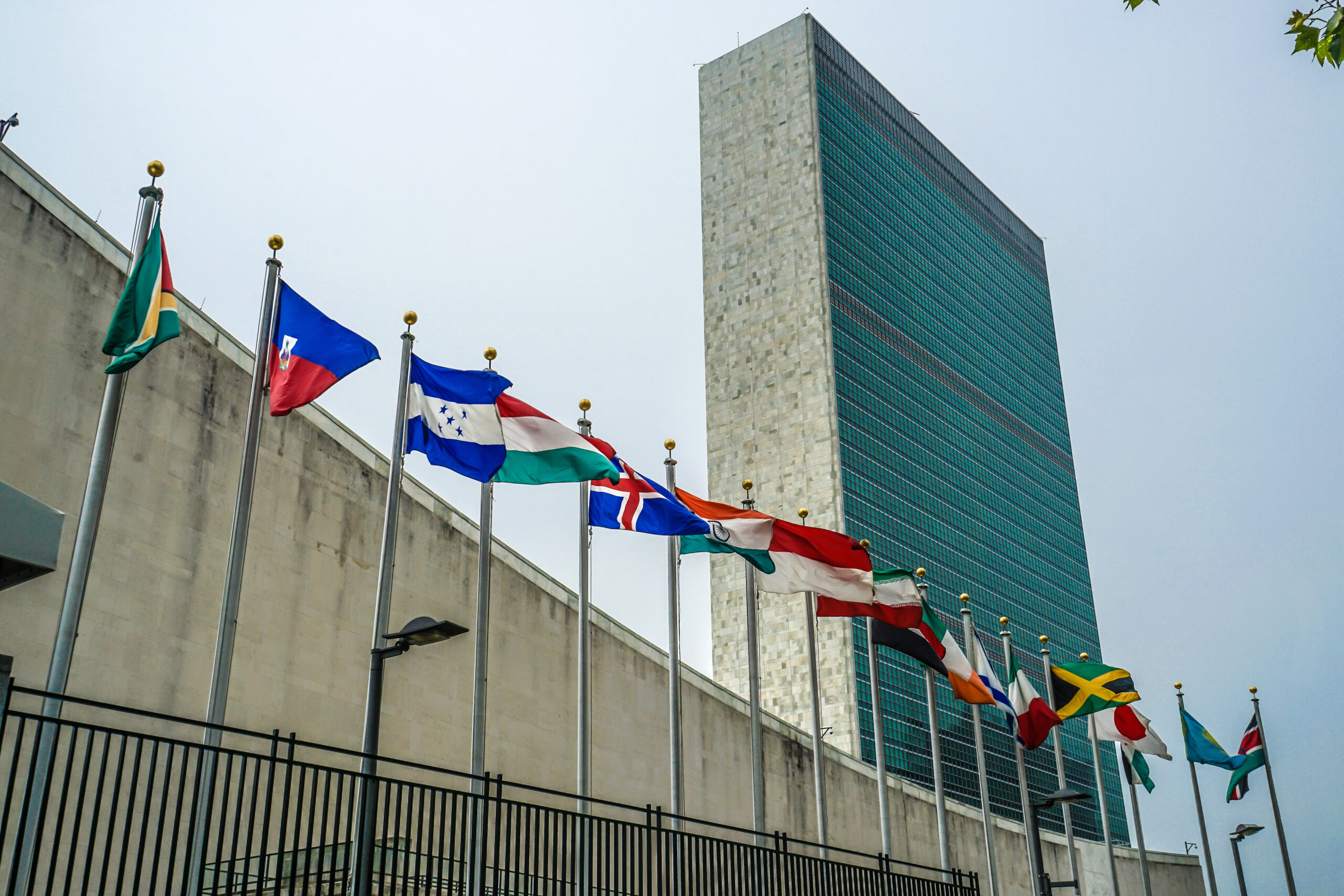 Exterior of a tall, rectangular building, with a line of colorful flags in front