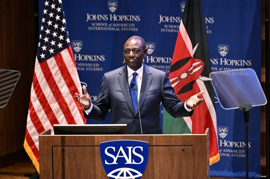 Kenyan President William Ruto speaks from a podium, with the flags of the United States and Kenya behind him.