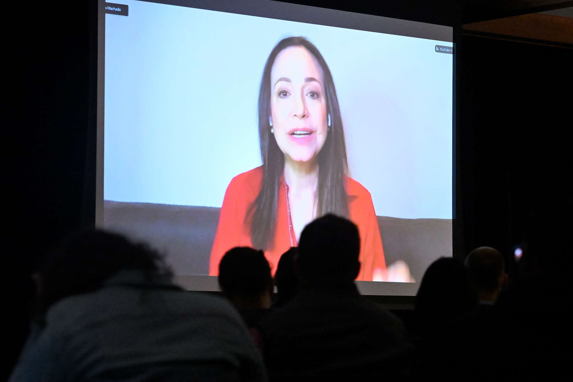 A woman in a red shirt appears on a large video screen