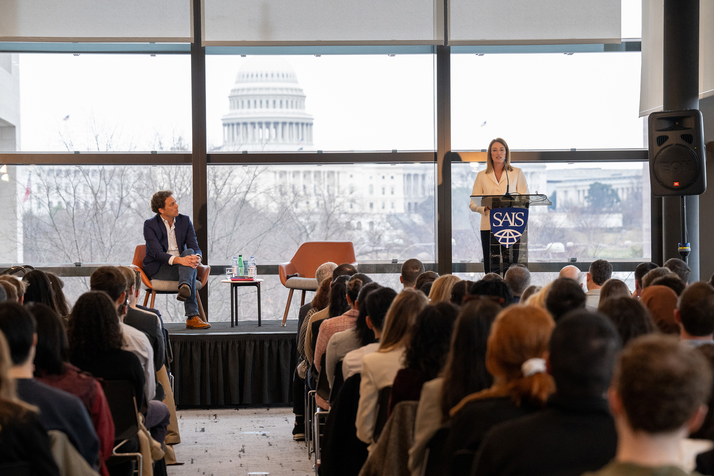 A speaker addresses a large crowd; the U.S. Capitol dome is visible in the background